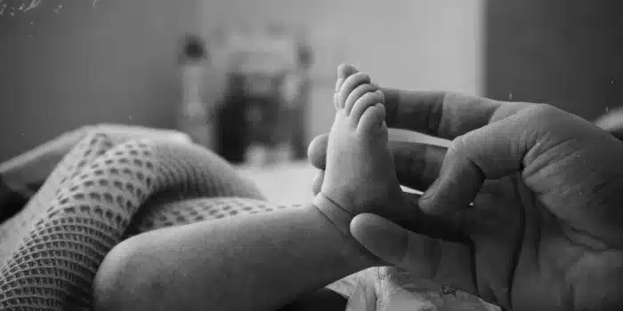 Parent tenant délicatement un nouveau-né dans une chambre au doux éclairage, avec des mouchoirs et une tasse à proximité