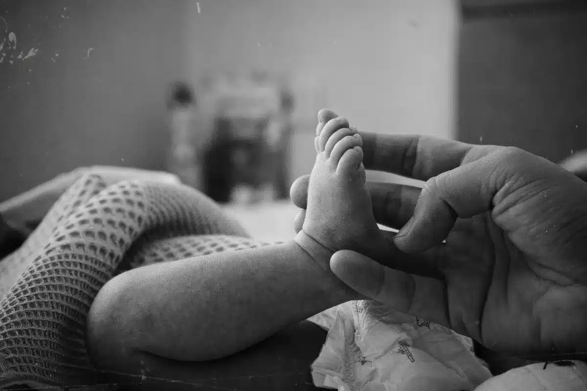 Parent tenant délicatement un nouveau-né dans une chambre au doux éclairage, avec des mouchoirs et une tasse à proximité