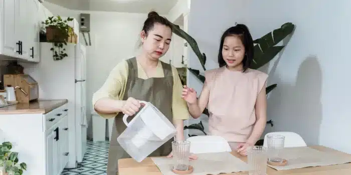 Verre d'eau fraîche versée sur un plan de travail ensoleillé avec légumes frais à proximité