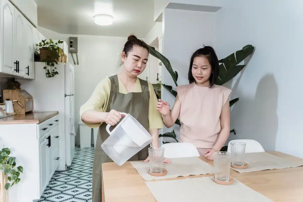 Verre d'eau fraîche versée sur un plan de travail ensoleillé avec légumes frais à proximité