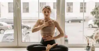 Personne assise près d'une fenêtre en lumière douce, respirant calmement dans un moment de réflexion sereine.