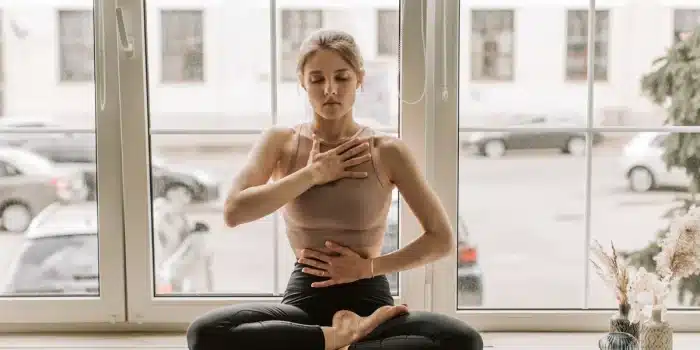 Personne assise près d'une fenêtre en lumière douce, respirant calmement dans un moment de réflexion sereine.