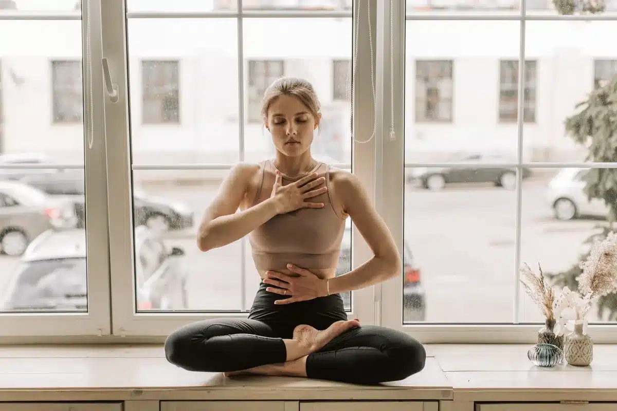 Personne assise près d'une fenêtre en lumière douce, respirant calmement dans un moment de réflexion sereine.