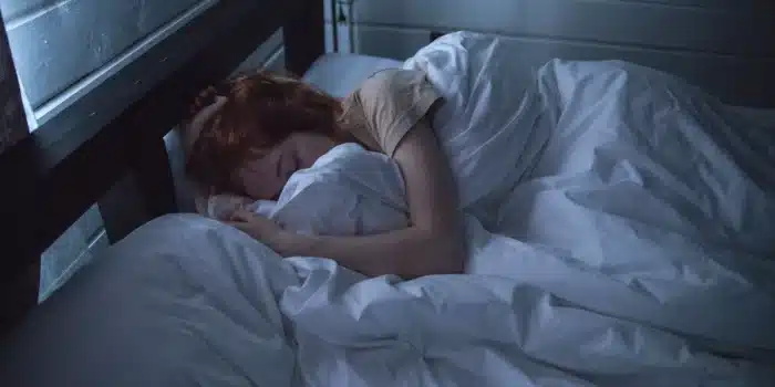 Personne au lit la nuit, tournée partiellement, bras sur l'oreiller, tension légère dans la posture, lumière chaude