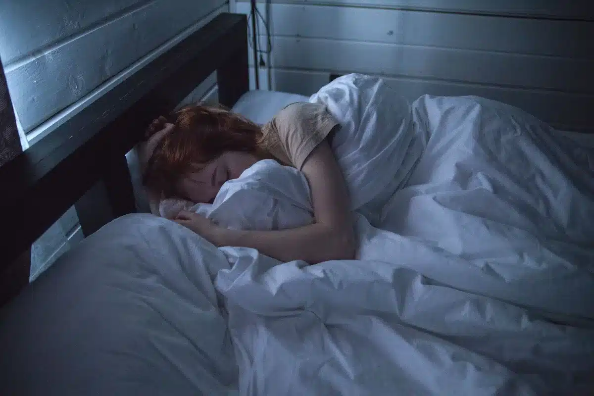 Personne au lit la nuit, tournée partiellement, bras sur l'oreiller, tension légère dans la posture, lumière chaude