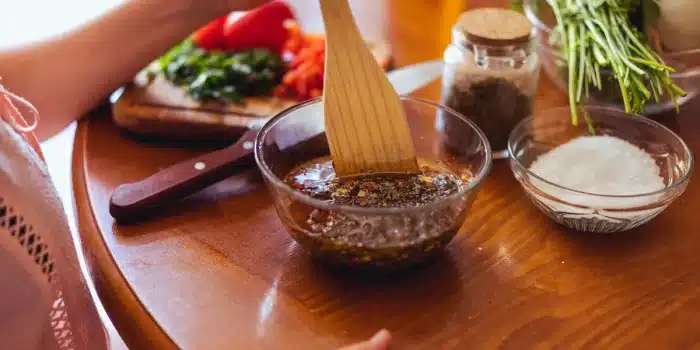 Préparation d'huile pimentée maison : versement d'huile d'olive dans un bocal avec piments séchés et herbes