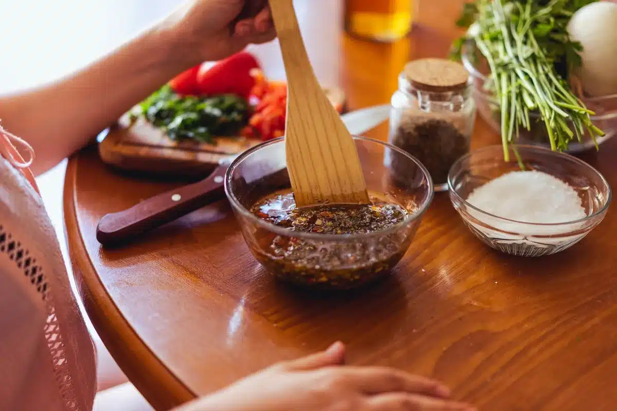 Préparation d'huile pimentée maison : versement d'huile d'olive dans un bocal avec piments séchés et herbes
