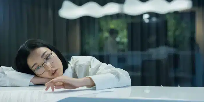 Personne fatiguée assise à un bureau, la tête appuyée sur sa main, regardant par la fenêtre