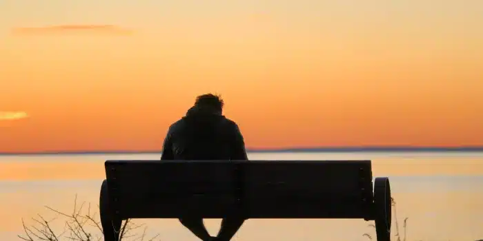 Silhouette d'une personne isolée, visage tourné, entourée de figures familiales floues en arrière-plan.