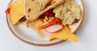 Mains préparant un taco végétarien garni de haricots, poivrons et herbes fraîches