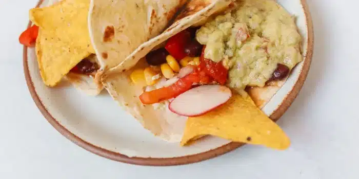 Mains préparant un taco végétarien garni de haricots, poivrons et herbes fraîches