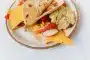 Mains préparant un taco végétarien garni de haricots, poivrons et herbes fraîches