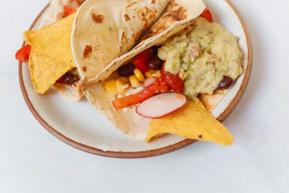 Mains préparant un taco végétarien garni de haricots, poivrons et herbes fraîches