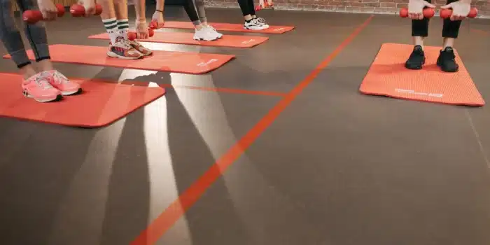 Personne en cours collectif de fitness, levant les bras dans une ambiance de groupe énergique.