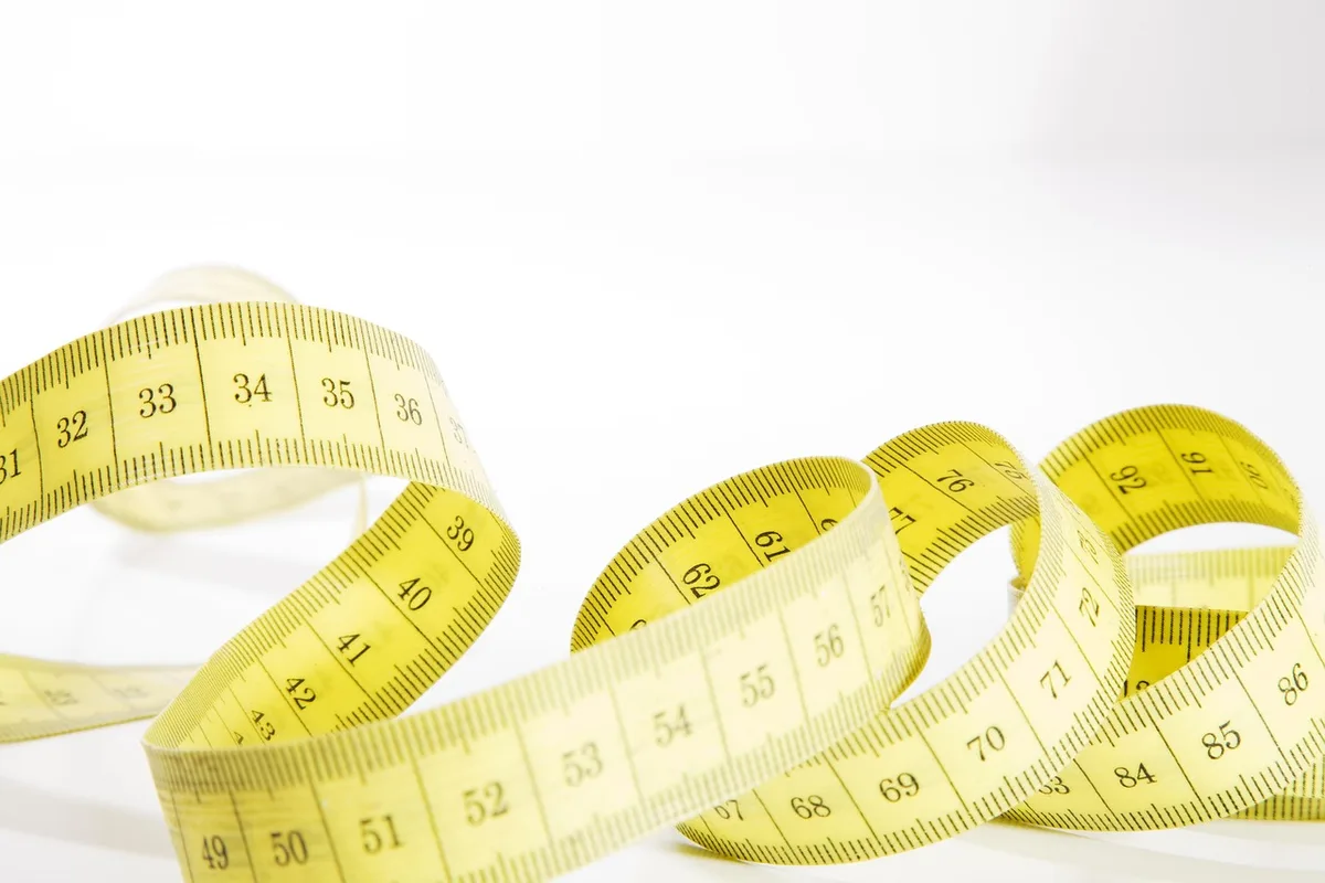 Personne mesurant son tour de taille avec un mètre ruban en intérieur lumineux