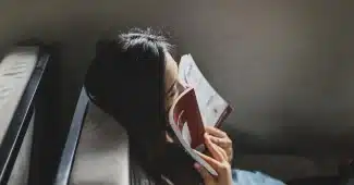 Une personne assise seule, écrivant dans un journal avec un stylo, dans une pièce calme baignée de lumière naturelle.
