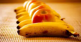 Blender sur un plan de travail en journée, bananes et framboises prêtes à être mixées
