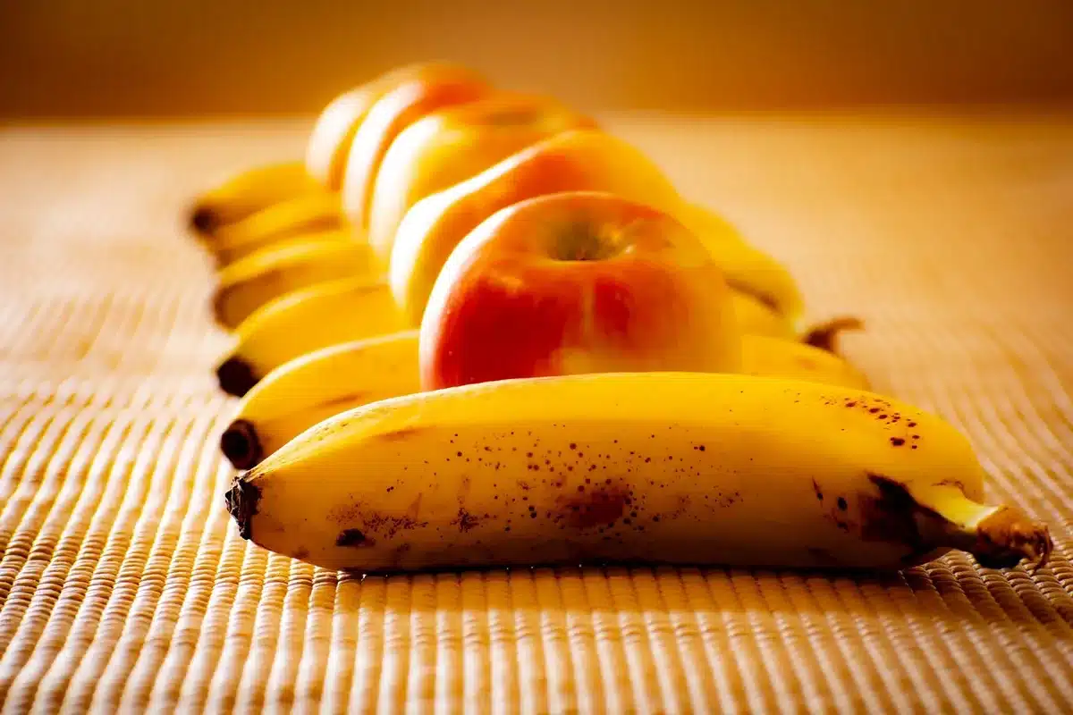 Blender sur un plan de travail en journée, bananes et framboises prêtes à être mixées